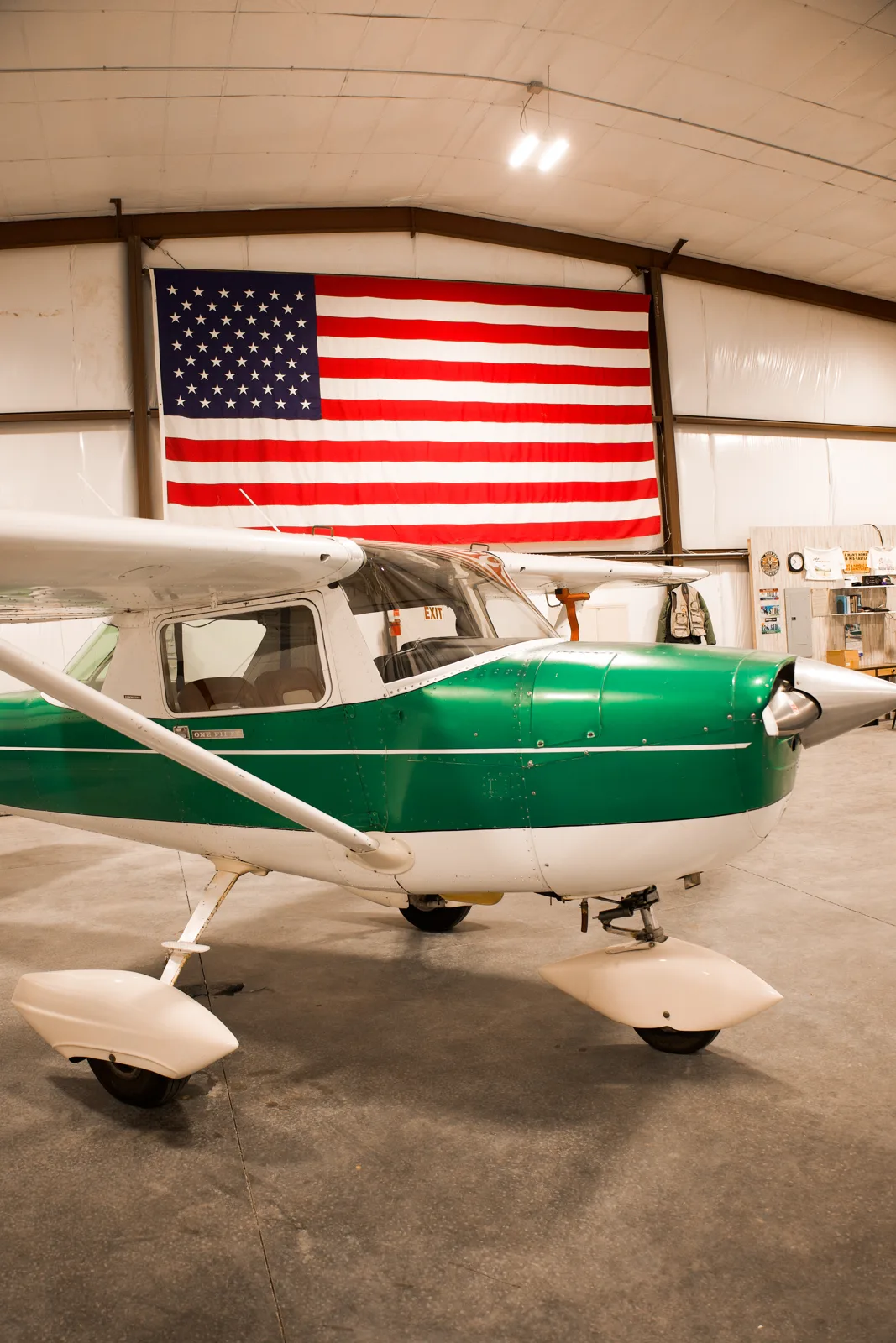 Vintage green Cessna nose-on in the hangar with a large American flag